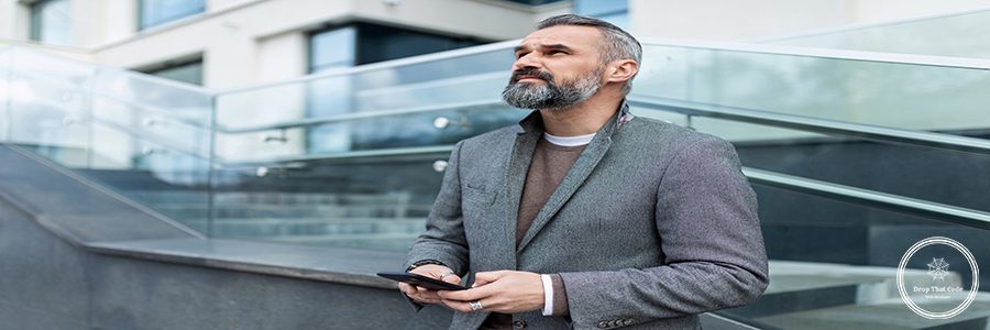 adult confident businessman With a slight smile on his face looks up with a mobile phone in his hands on the background of a business center.