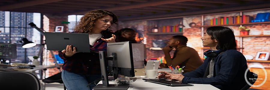Startup intern holding laptop asks questions to senior technician coding advanced AI algorithm. Employee requests help from CTO manager in Silicon Valley workplace, camera B