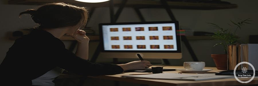 Back view image of concentrated young lady designer sitting indoors using computer and graphics tablet.