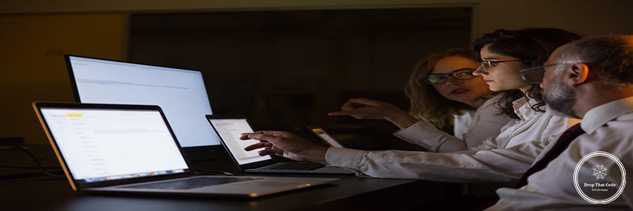 Business people discussing work in dark office. Professional male and female business colleagues looking at laptop computer screen and discussion project late at night. Business and technology concept