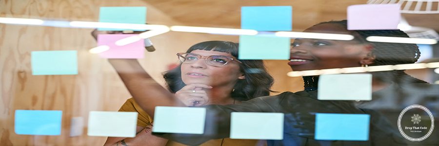 Business people, thinking and planning with notes in a creative office for designer project. Women team together for collaboration, teamwork and ideas on a glass wall with color paper and diversity.