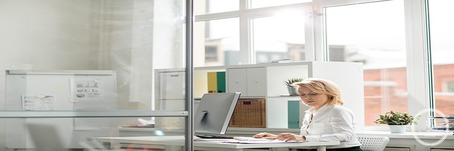 Serious office worker concentrating on reading documents by her workplace
