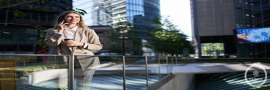 Corporate woman stands on street in city center, has a phone call, telephone conversation, smiling and drinking coffee.