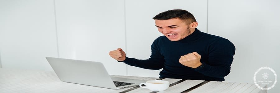 Excited happy man showing fists, celebrate his success after winning online. At home.