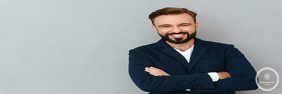 Happy bearded man in business clothes with crossed arms looking at the camera over gray background