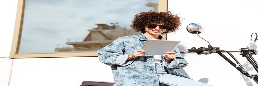 Happy young woman in sunglasses using tablet computer while sitting on a motorbike outdoors