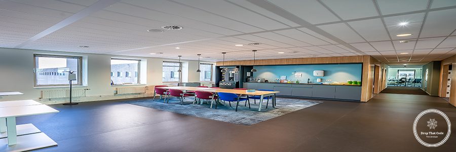 The interior of the kitchen area of a modern office with a long wooden table and chairs