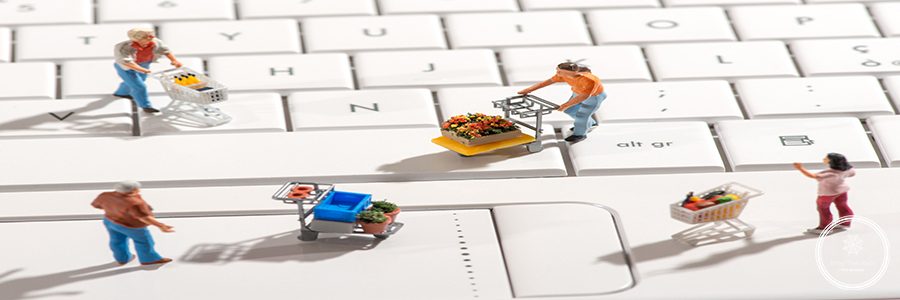 Four different miniature people with shopping carts on a white computer keyboard viewed high angle with shadows in a concept of online or internet shopping