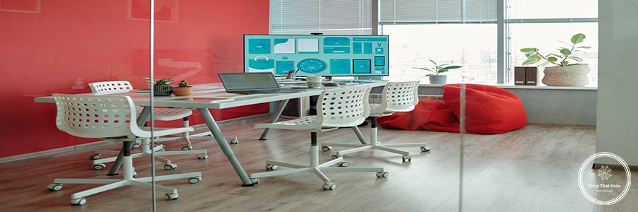 Modern office meeting room with red wall, large screen, and white chairs, featuring table with laptop and coffee cup