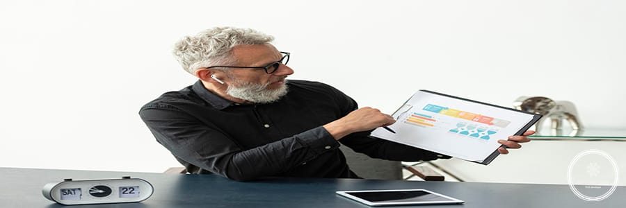 older-man-home-showing-graph-notepad-with-tablet-desk