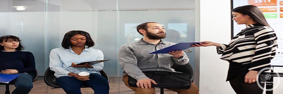 Female recruiter taking cv resume from bearded man as other job applicants wait in the office lobby. Asian woman receiving clipboard and asking male candidate to enter the recruitment meeting room.