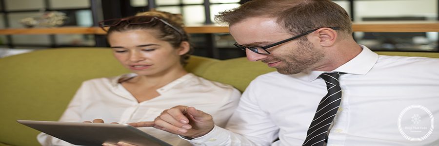 Relaxed coworkers chatting and using tablet in office lobby. Business man and woman sitting on couch and holding tablet computer. Business colleagues concept.