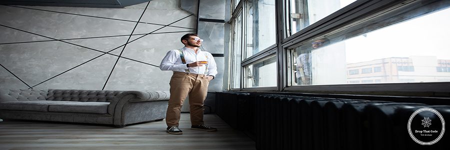 Success concept. Stylish young bearded man is standing near the window and looking far. He is in a suit, pensive and concentrated