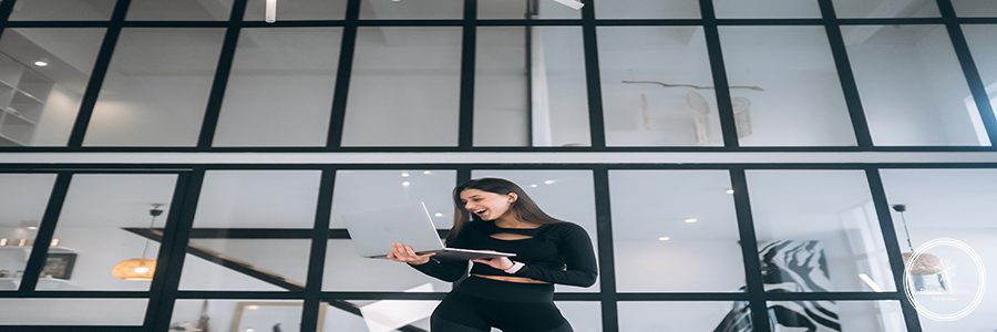 Young woman in a sports suit standing holding a laptop in her hands at home