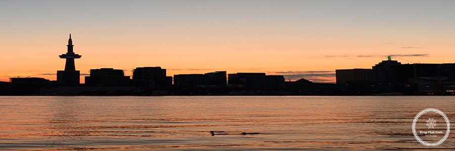 Toronto city skyline silhouette at sunset over lake with urban skyscrapers.