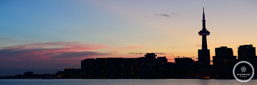 Toronto city skyline silhouette at sunset over lake with urban skyscrapers.
