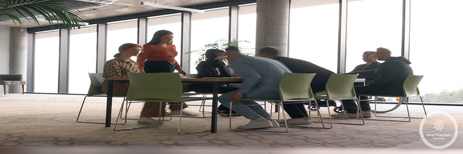 A diverse business team, working urgently around a conference table, collaborates on a meeting while their director, seated in a wheelchair, waits for their input.
