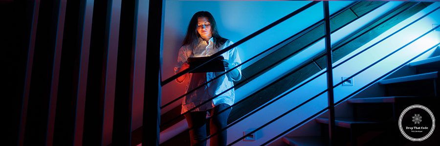 Woman using tablet computer while standing on a stairway indoors at home at night